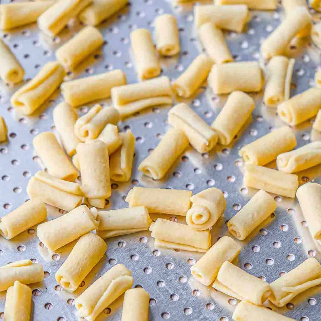 A lot of handmade macaroni evenly spaced on a perforated metal tray.