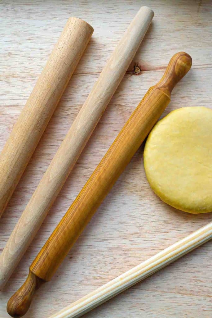 Different sizes of rolling pins encircling a round yellow ball of semolina pasta dough.