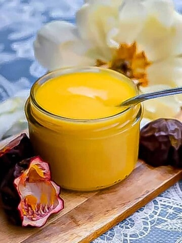passionfruit curd in a jar sitting on a cutting board with some passionfruit peels and a large flower in the background.