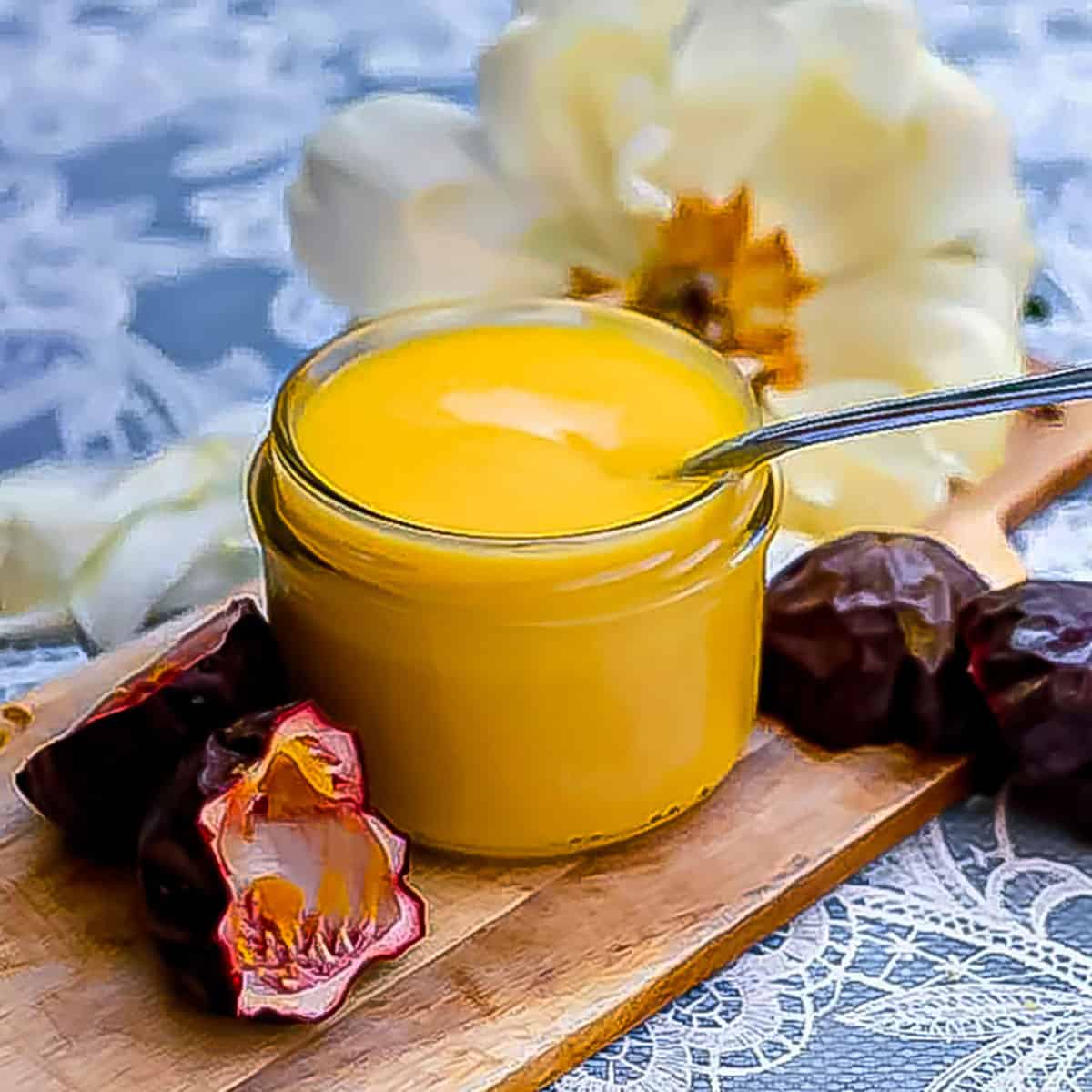 passionfruit curd in a jar sitting on a cutting board with some passionfruit peels and a large flower in the background.