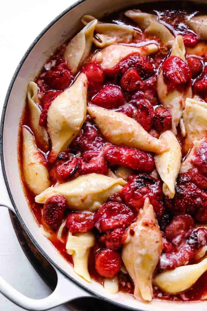 A large pot of creamy pasta shells cooked in milk syrup and drizzled in maple roasted strawberries.