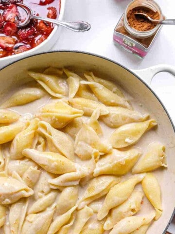 A big pot of large pasta shells slow cooked in milk and sugar until creamy. There is also a side dish of roasted strawberries and a pot of cinnamon.