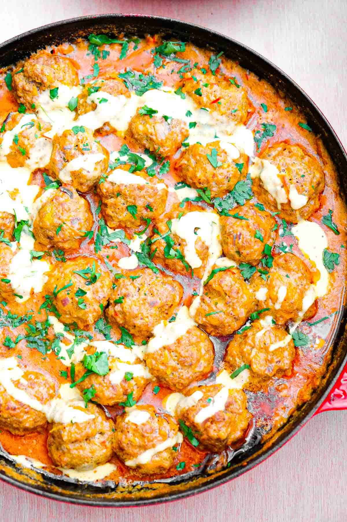An overhead view of the coconut curry meatballs in the sauce with a circular swirl of coconut cream and cilantro on top.