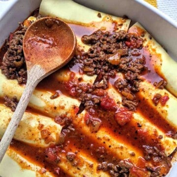 Lasagna with meaty berbere sauce being spooned onto it.
