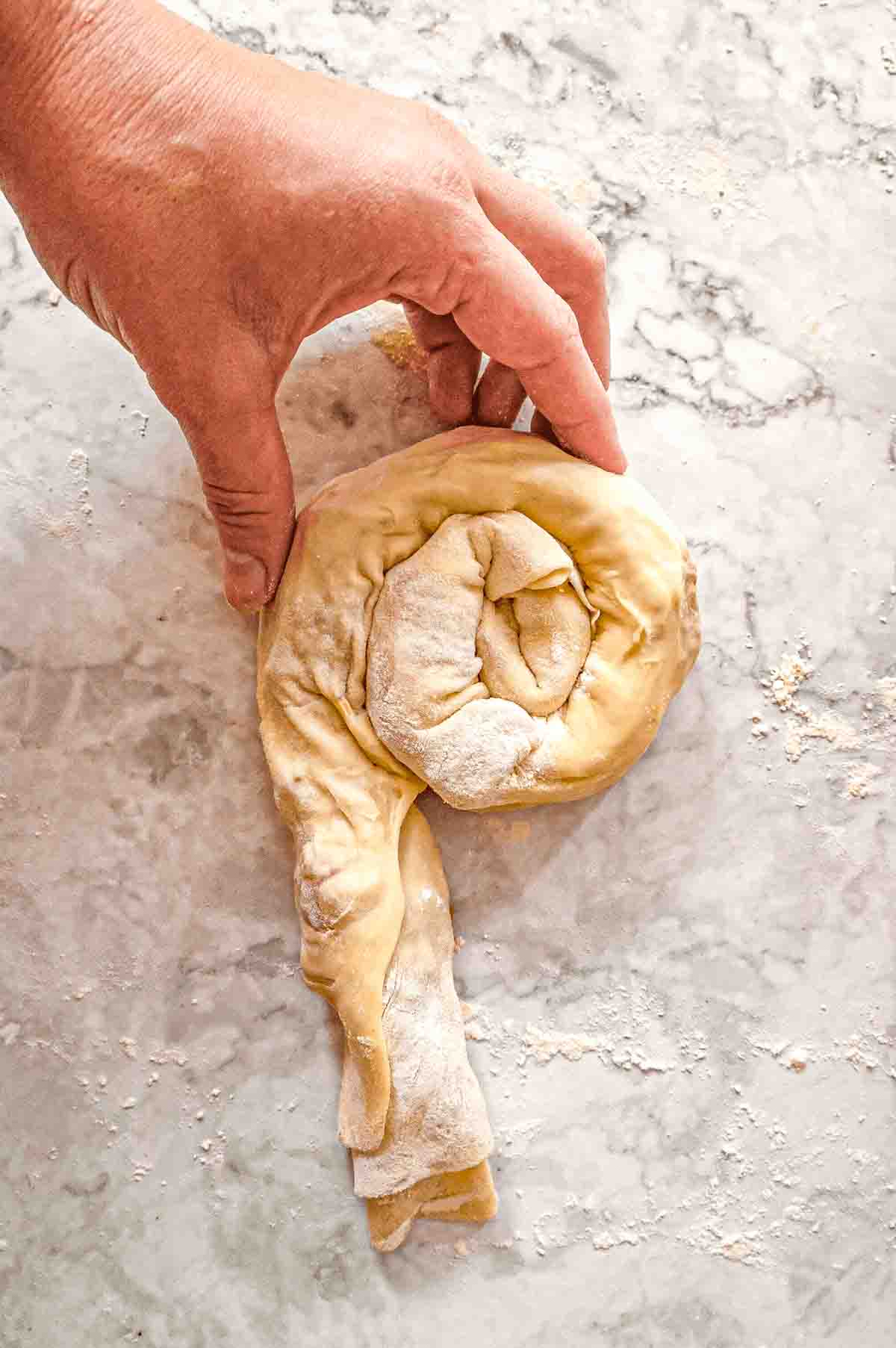Step three of rolling out and filling phyllo dough: The stuffed phyllo dough carpet or cigar shape is being rolled into a spiral bun shape.