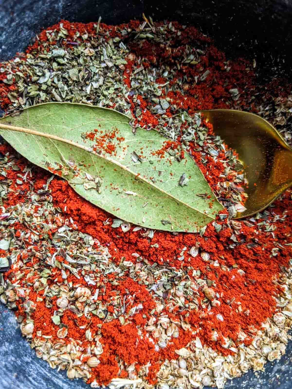 Berbere spice in the process of being ground in a mortar and pestle; a whole bay leaf is visible.