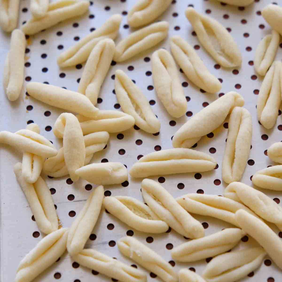 A pile of hand shaped cavatelli pasta drying on a perforated metal tray.