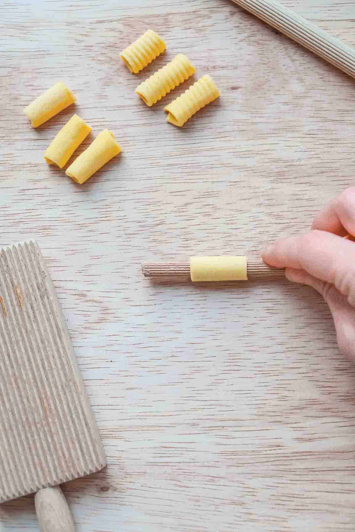 A square of pasta dough has been rolled into a tube on a ridged wooden dowel.