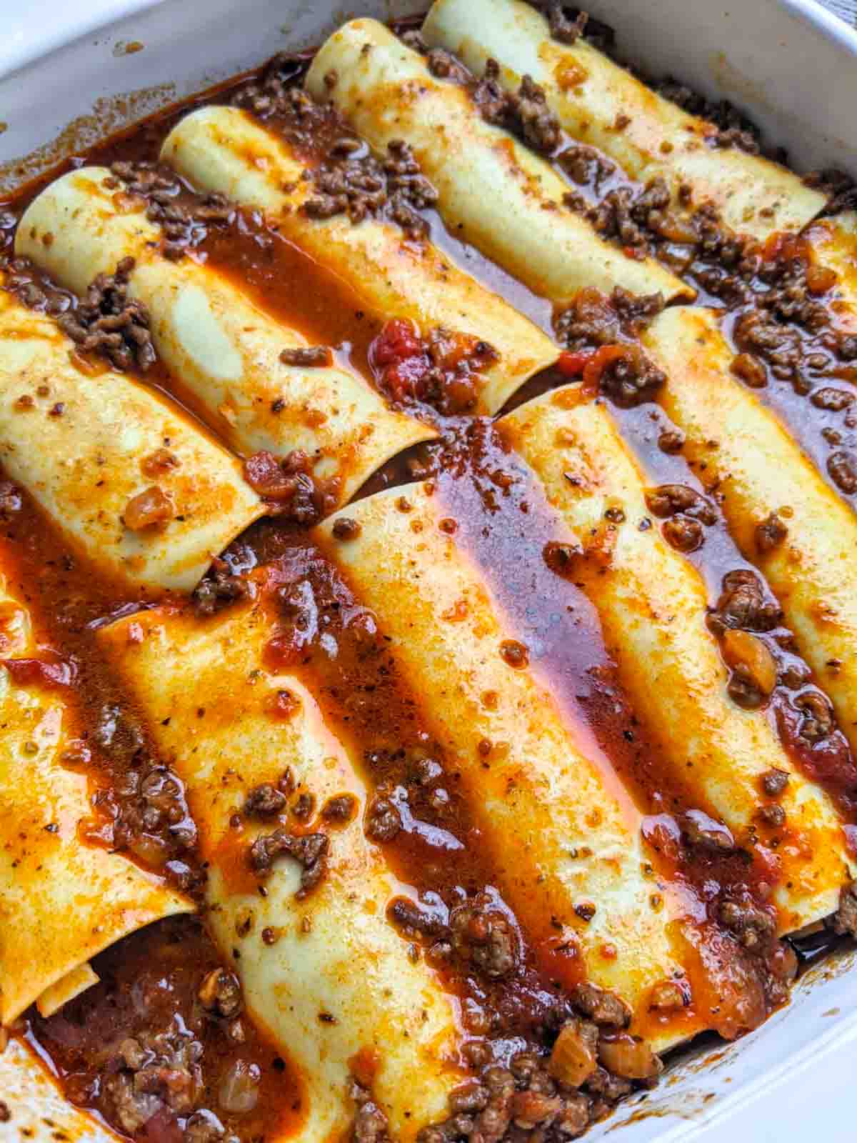 The filled lasagna noodles covered with sauce in a casserole dish.