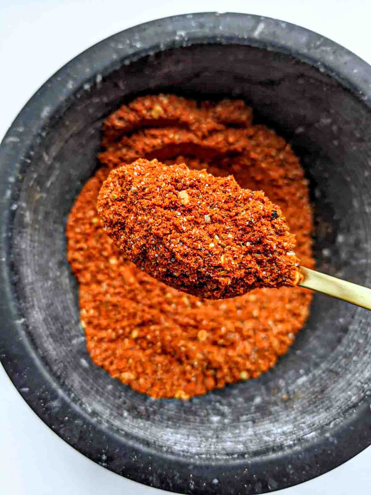 Finely ground berbere spice in a spoon after being ground in a mortar and pestle.