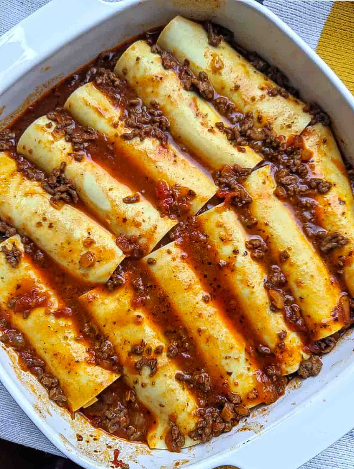 The lasagna noodles filled as tubes and laid out in a casserole dish in two rows. They are covered with meat sauce.