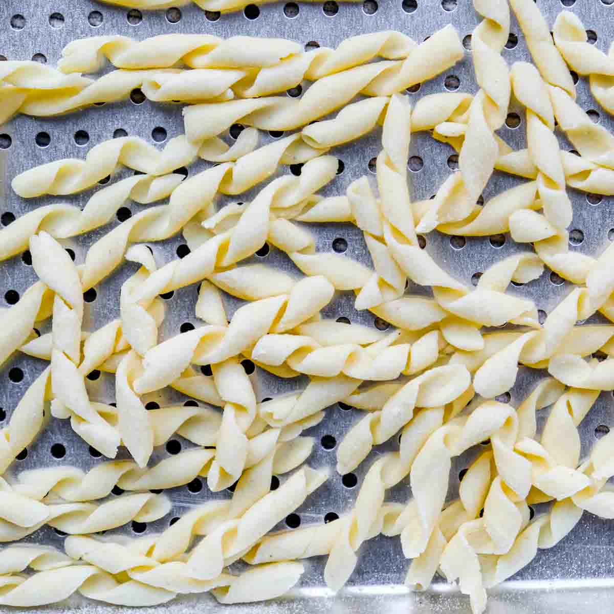 A bunch of homemade fusilli pasta drying on a perforated metal tray.