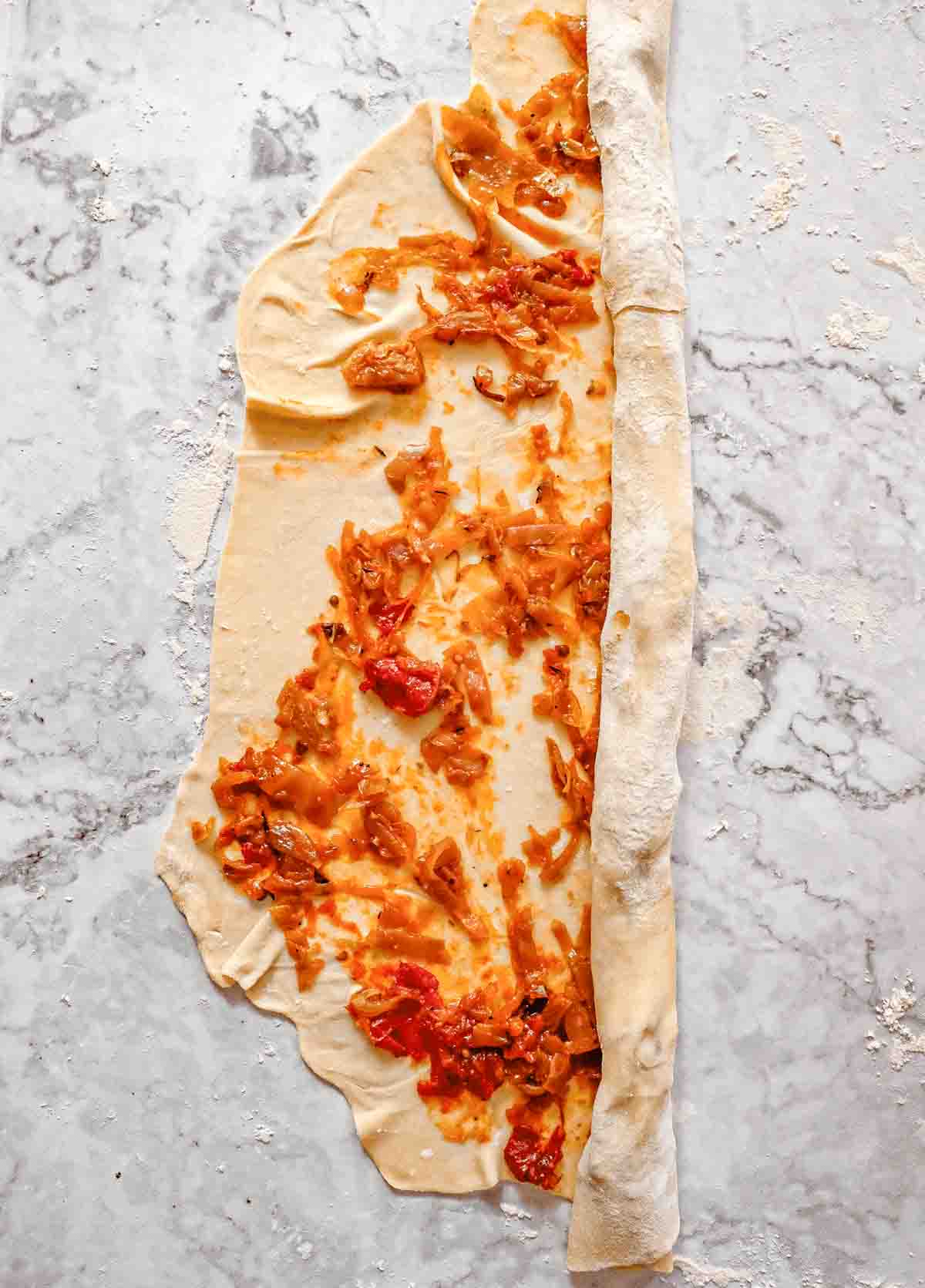 Step two of rolling out and filling phyllo dough: A thinly rolled out sheet of dough that has been covered with orange roasted cabbage and is being rolled into a carpet or cigar like shape.