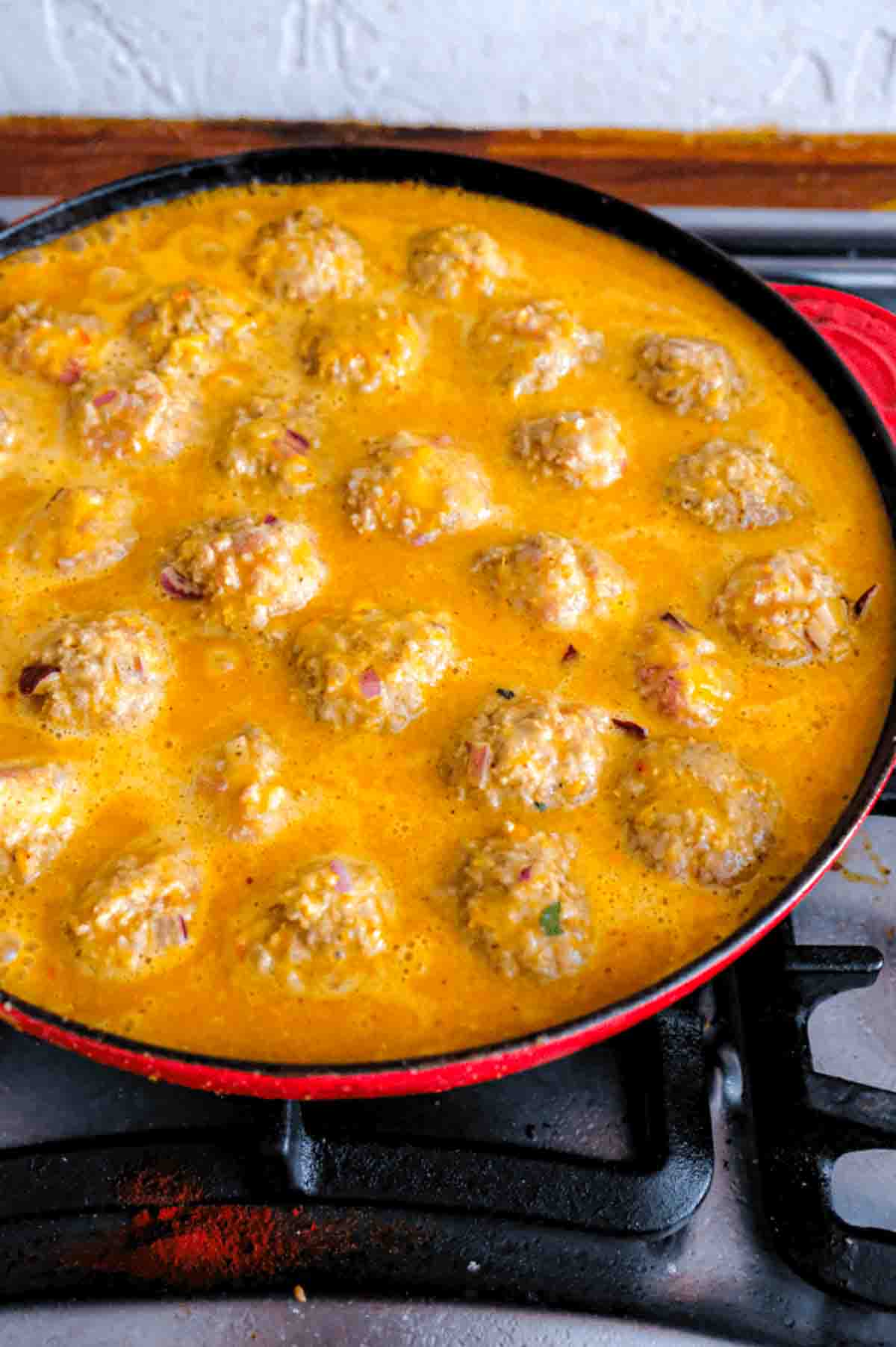 The now cooked meatballs simmering in a skillet in an orange curry sauce.