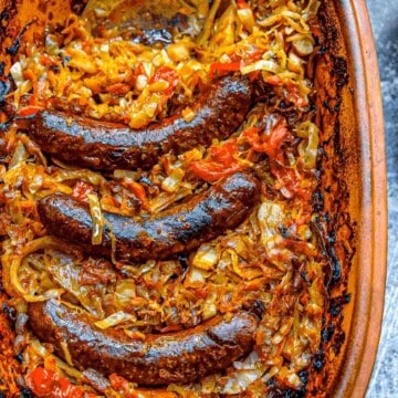 An overhead view of a clay pot full of slow roasted sauerkraut with browned sausages on top.