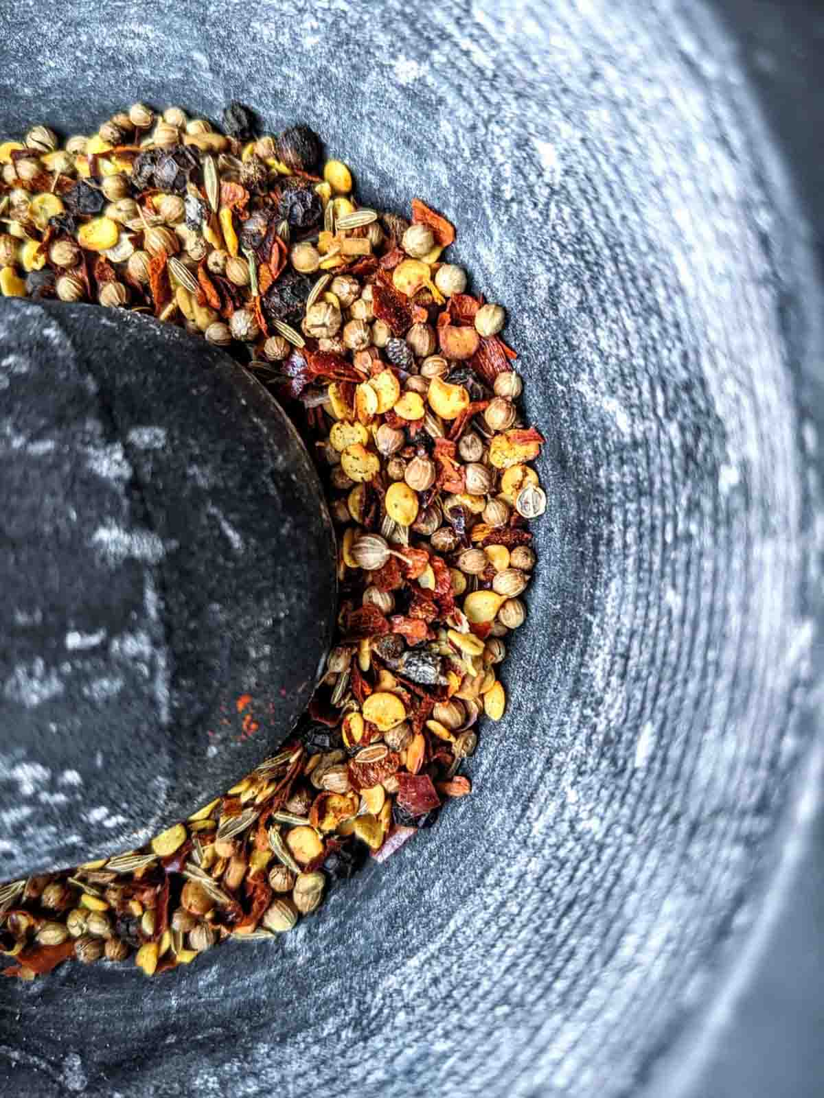 An overhead view of spices being ground in a stone mortar and pestle to make berbere spice.