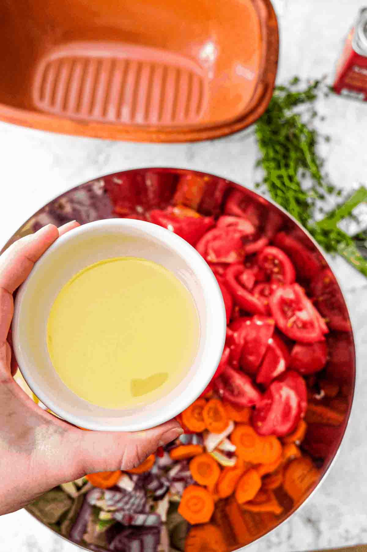 An overhead view of a small bowl containing one third of a cup of vegetable oil that is about to be poured into a larger bowl containing the ingredients for slow cooked cabbage.