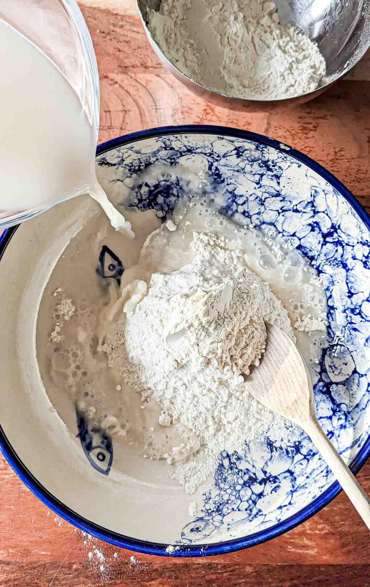 Pouring a yeast water mix over flour in a large bowl.