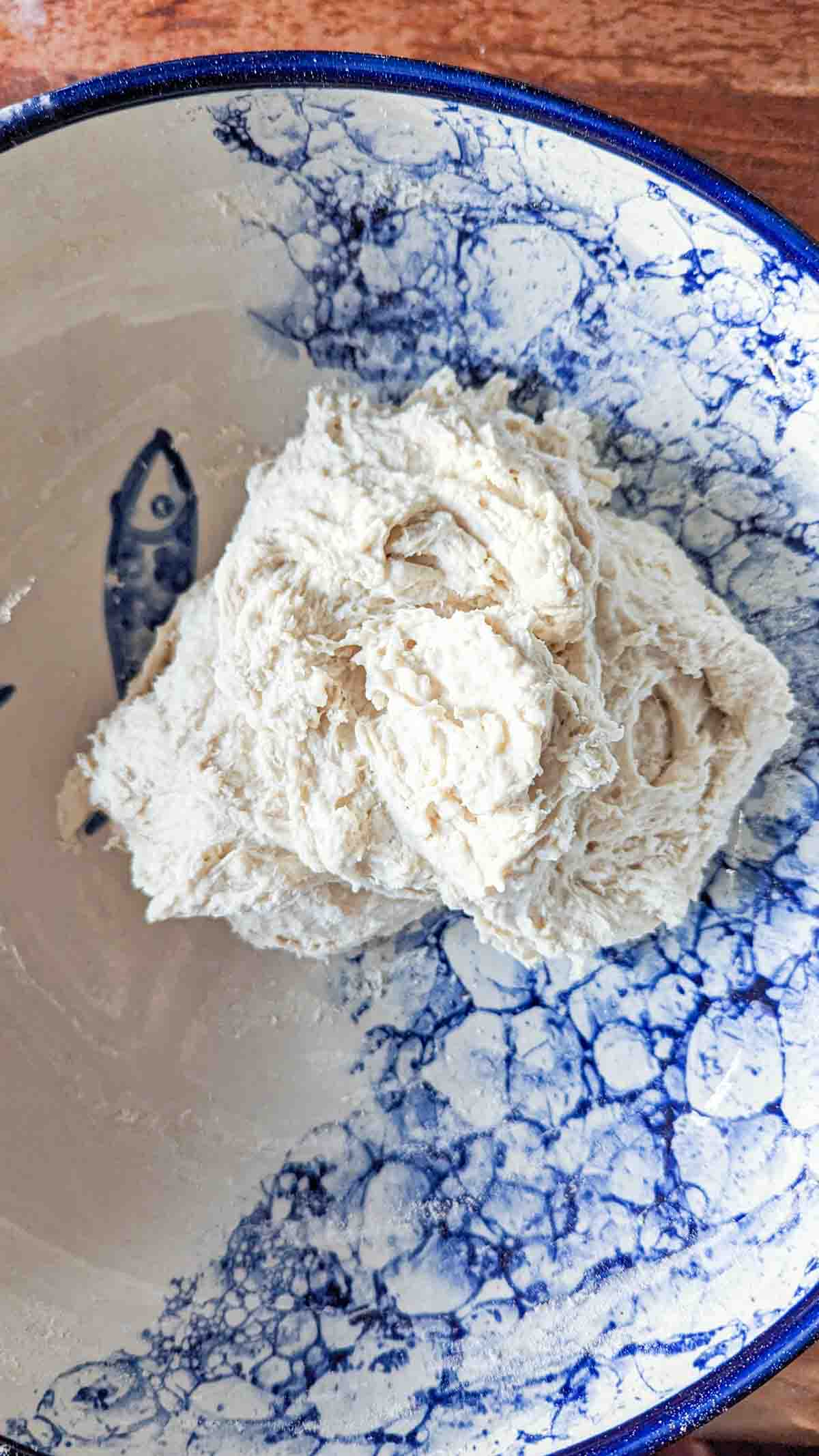 A ball of dough that's been mixed by hand sitting in a bowl.