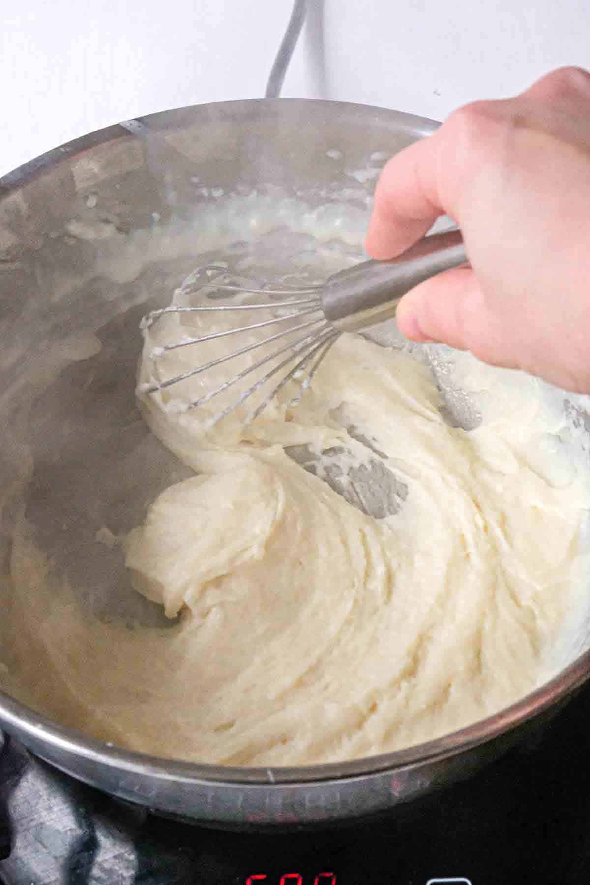 Whisking bechamel sauce while adding milk.