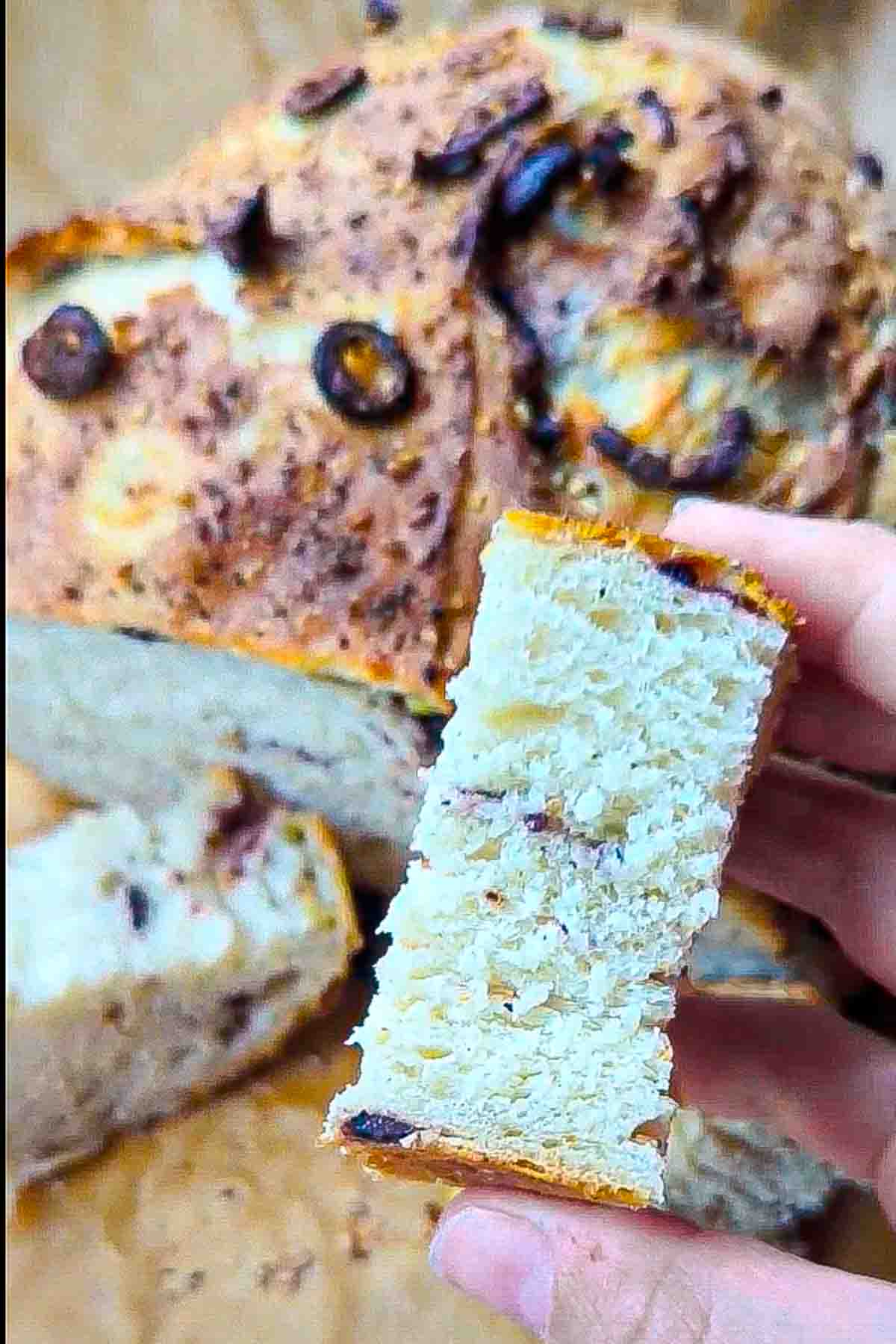 A slice of the sesame and olive bread being held up to show the soft crumb.