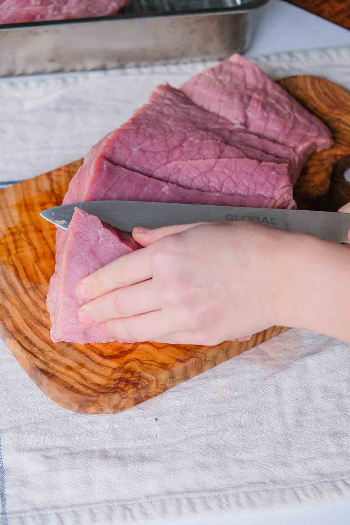 Making a series of cuts into a veal rump in order to flatten it out so it can be trussed.