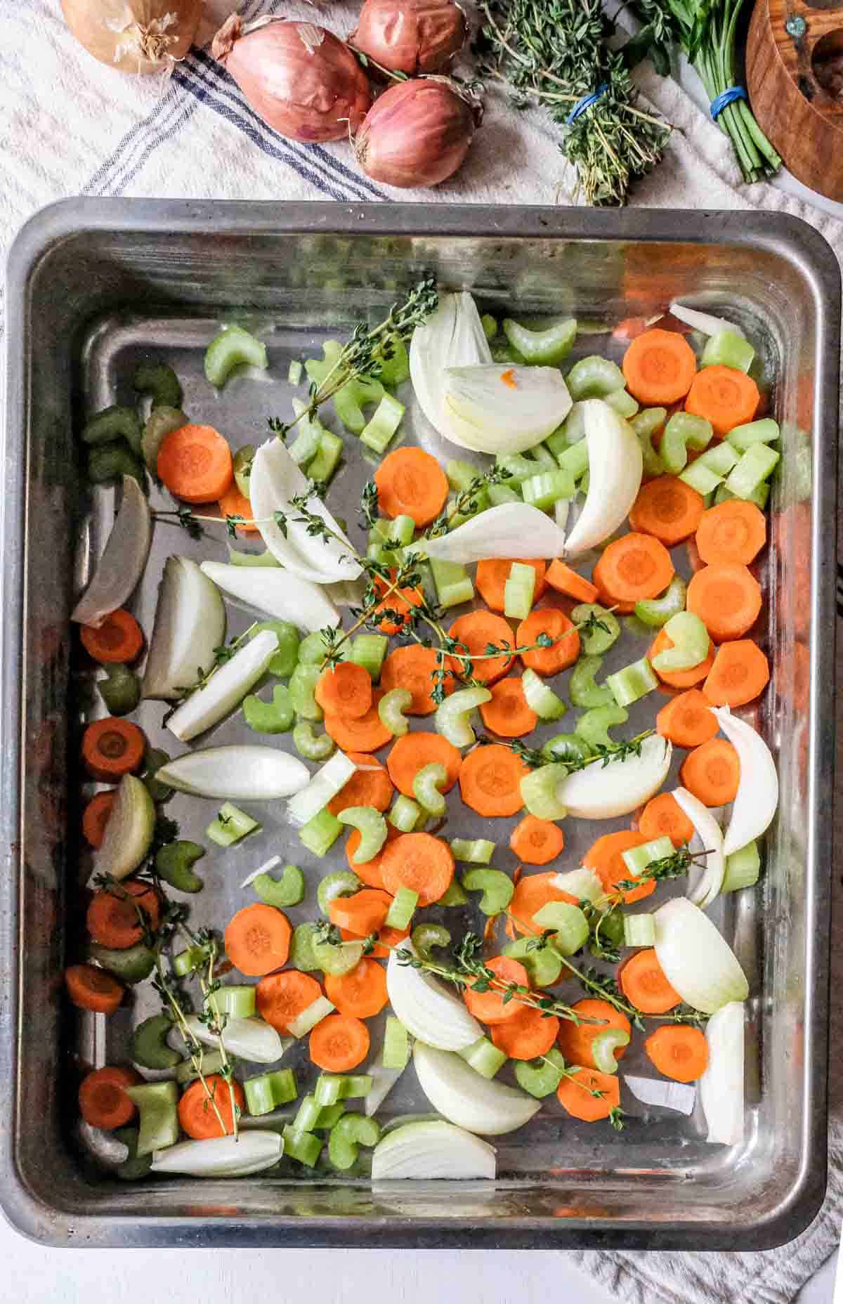 Carrots, celery, onions and thyme in a roasting pan.