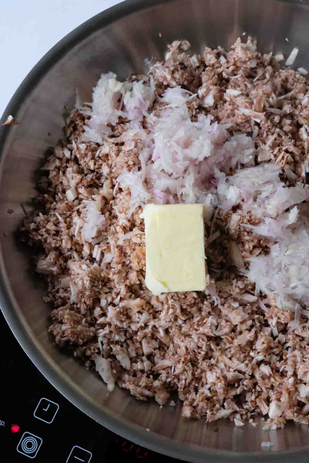 Finely chopped mushrooms cooking in a skillet with finely diced shallot as well as a knob of butter.