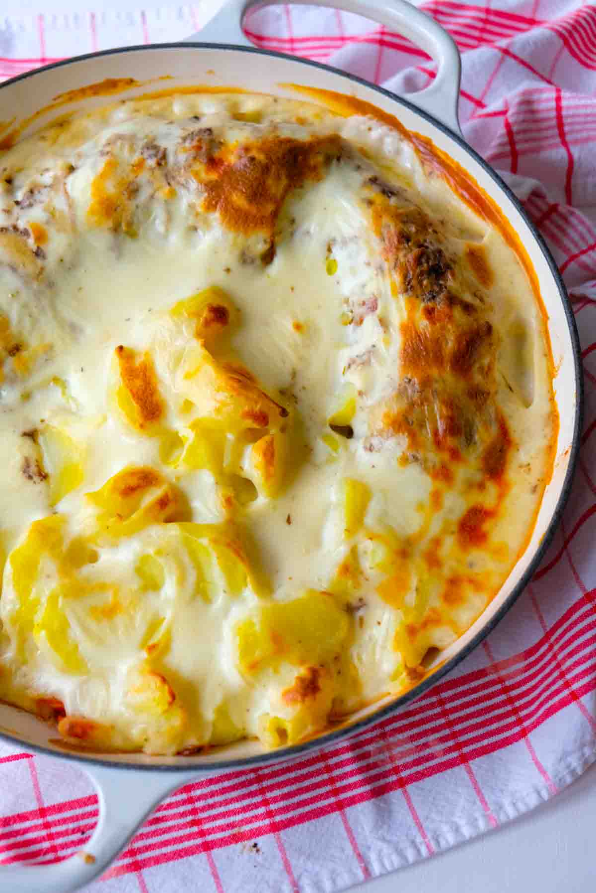 A cast iron casserole full of veal prince orloff and potatoes covered in Mornay sauce which has been baked to a golden finish.