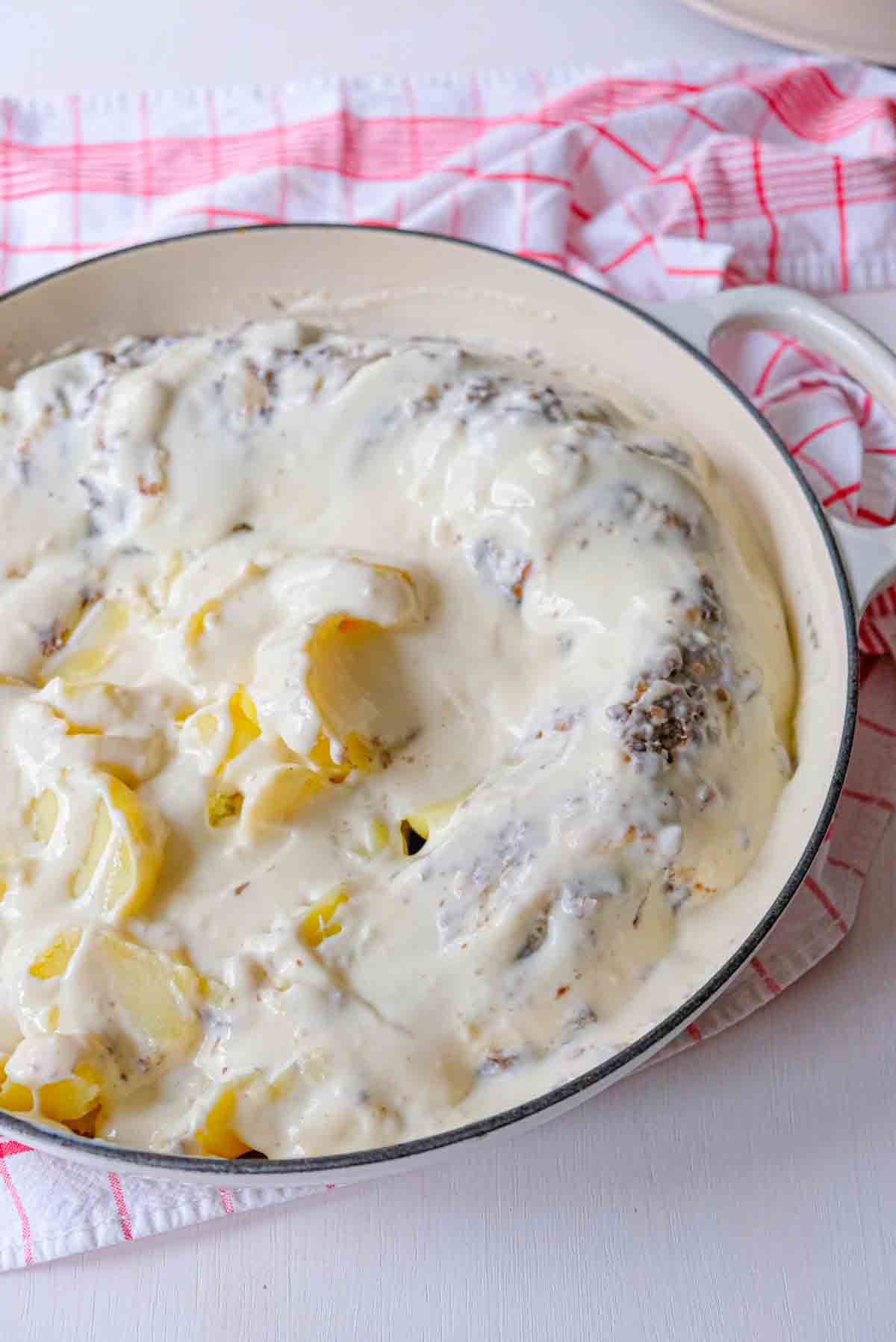 A cast iron casserole full of veal prince orloff and potatoes covered in white bechamel sauce.