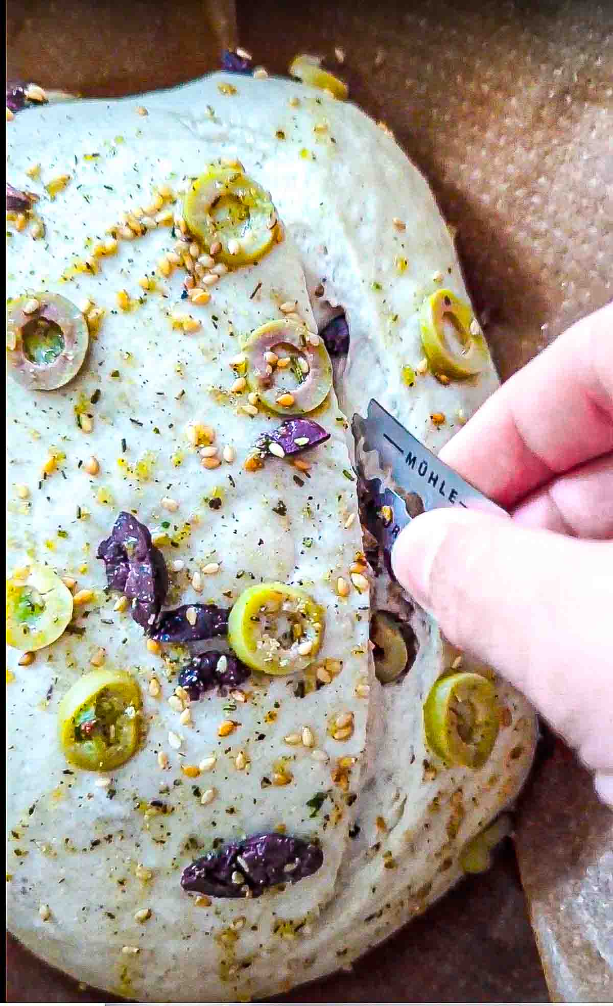 Using a razor blade to score the olive and sesame bread dough before baking.