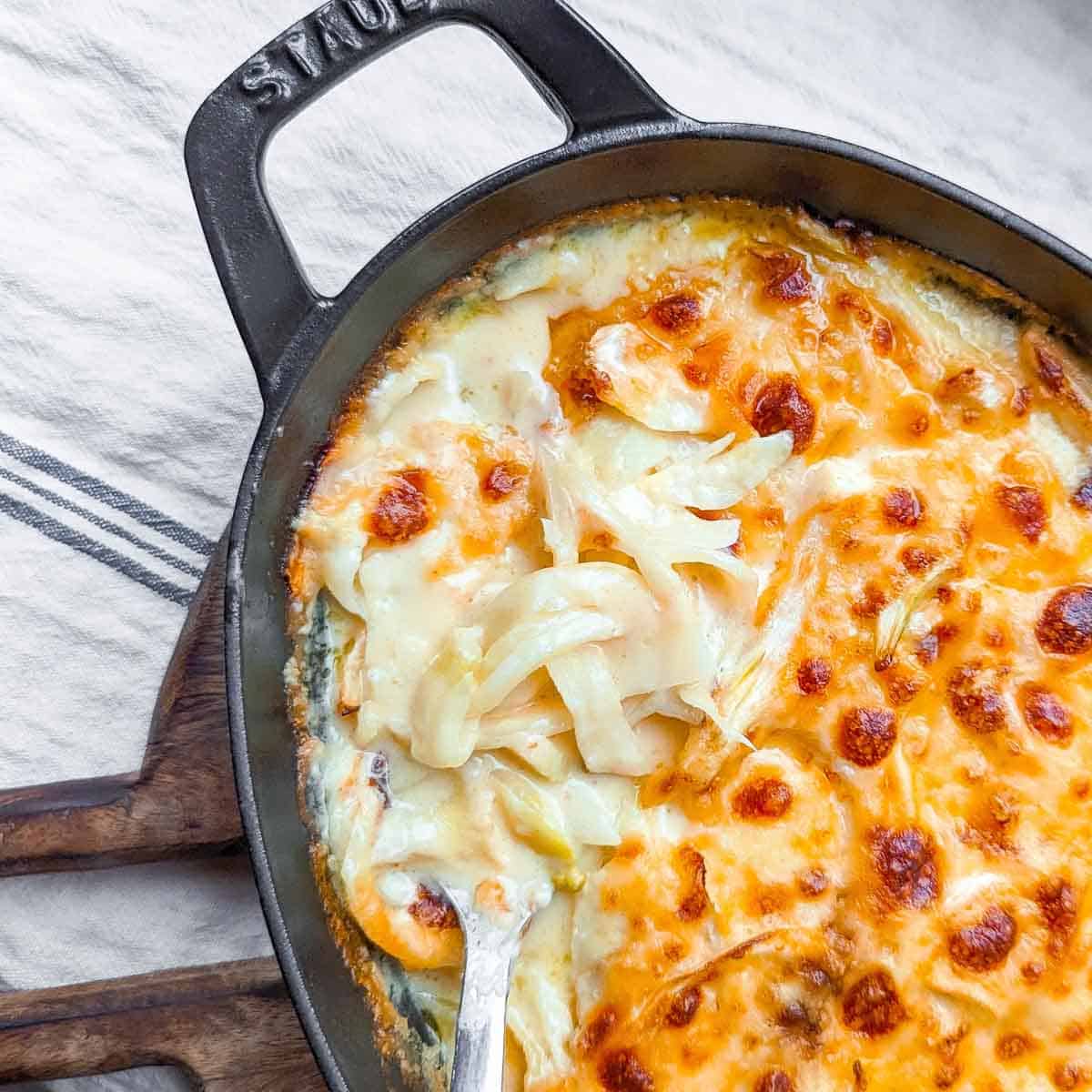 An overhead view of fennel gratin being spooned out of an oval cast iron roasting dish.