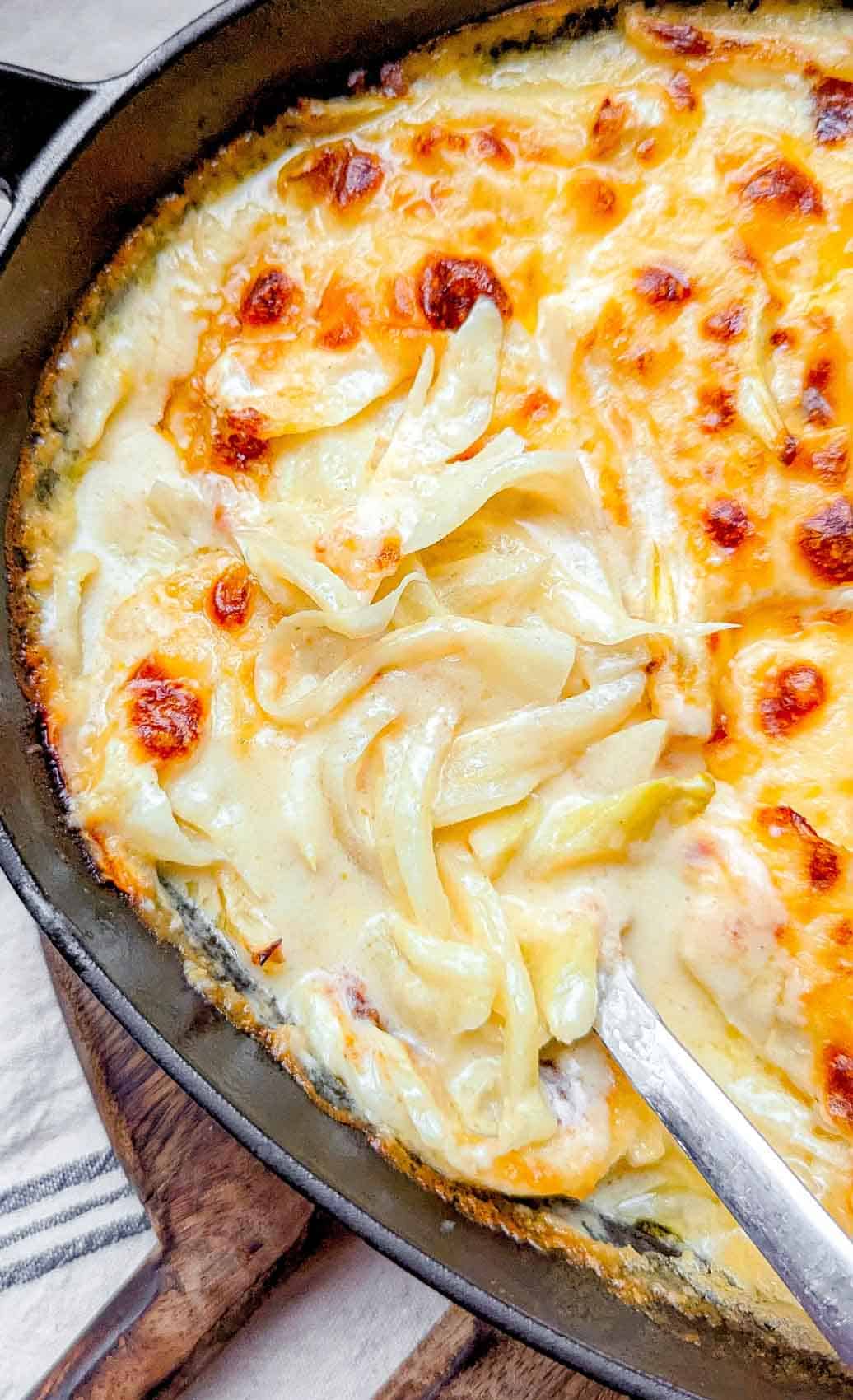 An overhead view of fennel gratin being spooned out of an oval cast iron roasting dish.