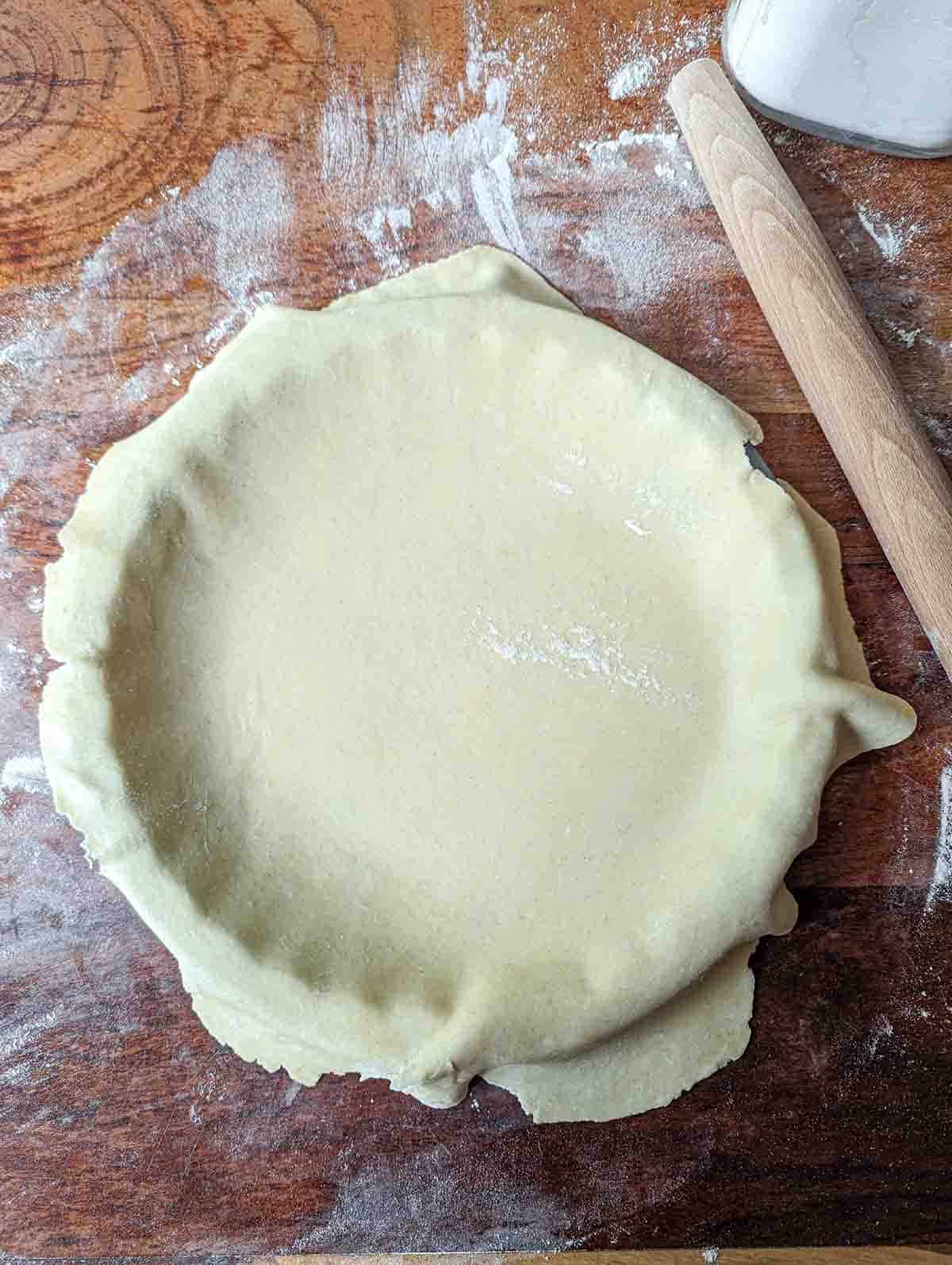 rolled out pie dough draped over a pie pan with a rolling pin off to the side