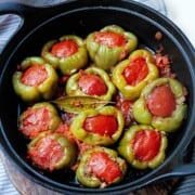 A cast iron pot full of stuffed peppers with tomato lids in tomato sauce.