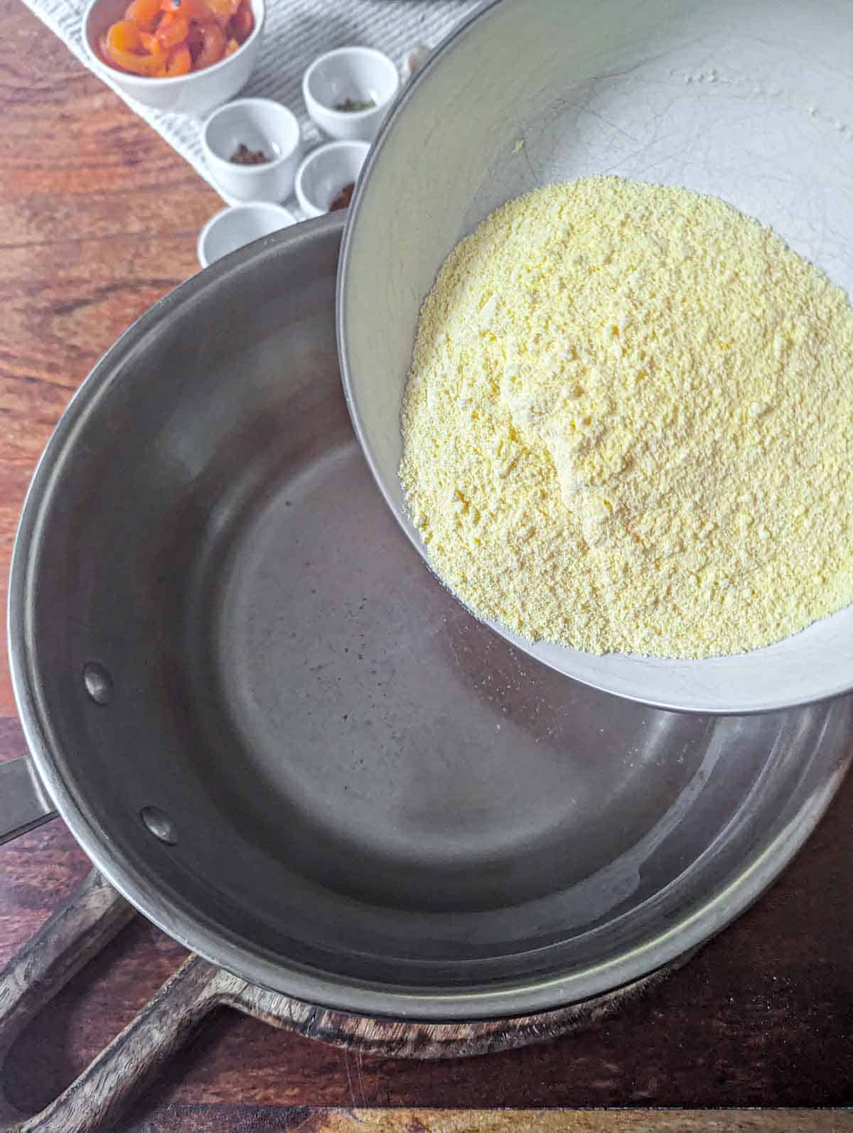 Adding dry cornmeal to simmering water in a saucepan.