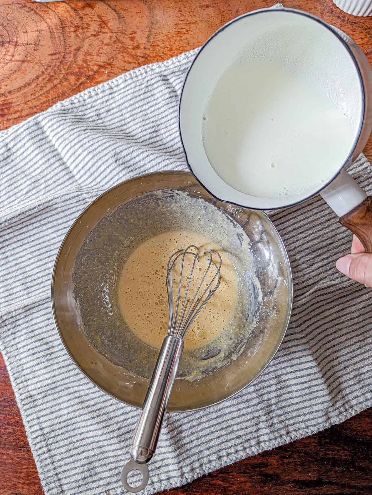 Pouring hot milk over blanched egg and sugar to make the pastry cream.