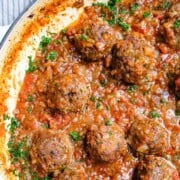 An overhead view of porcupine meatballs in tomato sauce garnished with fresh parsley.