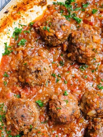 An overhead view of porcupine meatballs in tomato sauce garnished with fresh parsley.