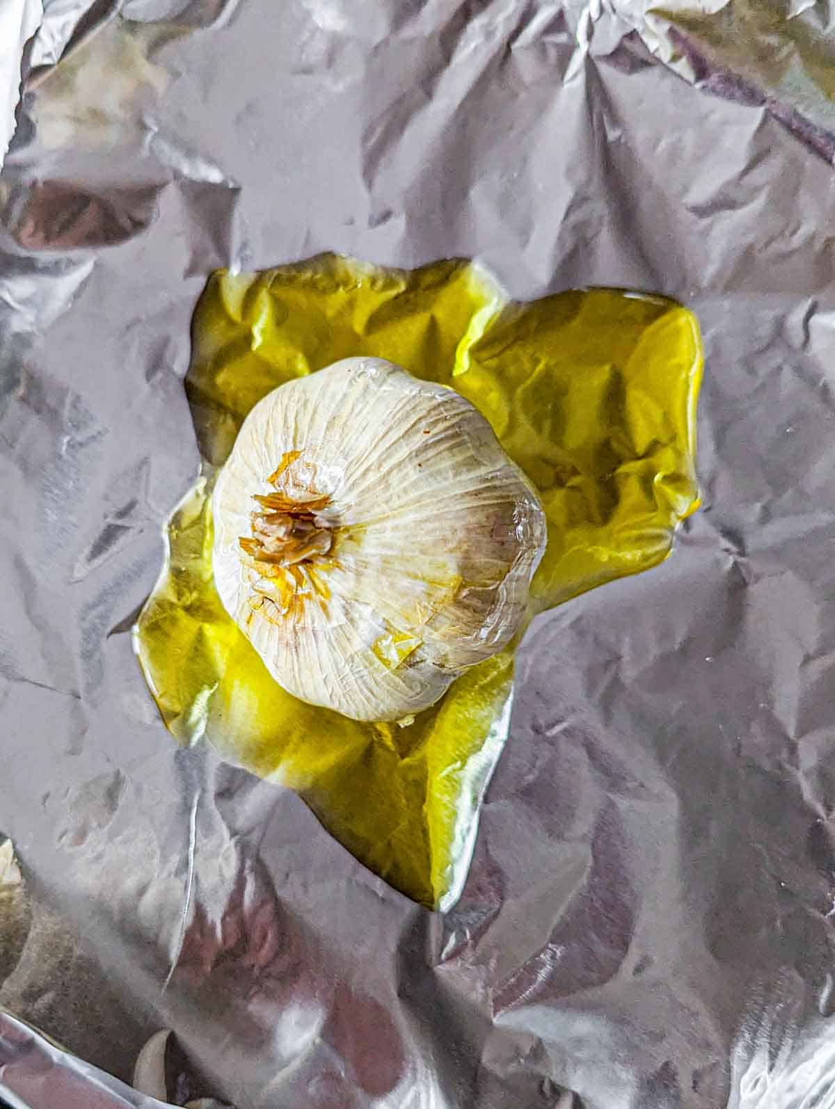 A garlic bulb on aluminum foil drizzled with olive oil.