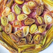 A close up overhead view of a ham and cheese leek tart with caramelized leeks cut into medallions in the center and lengthwise cut leeks around the edge.
