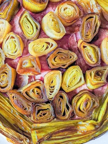A close up overhead view of a ham and cheese leek tart with caramelized leeks cut into medallions in the center and lengthwise cut leeks around the edge.