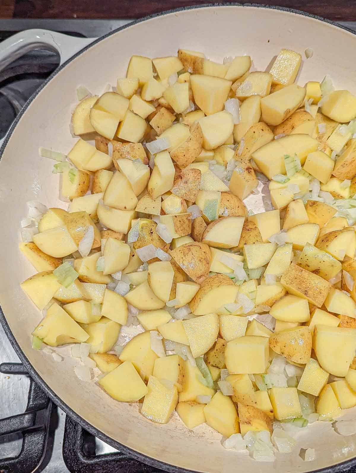 A large cast iron pot containing cubed potatoes and finely diced onions cooking in oil.