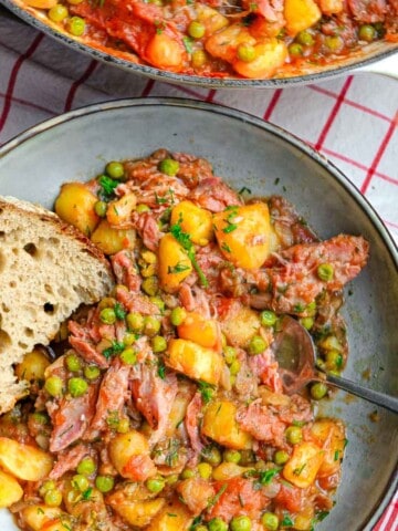 A plate of cooked potato stew with peas and smoked ham along with a slice of bread.