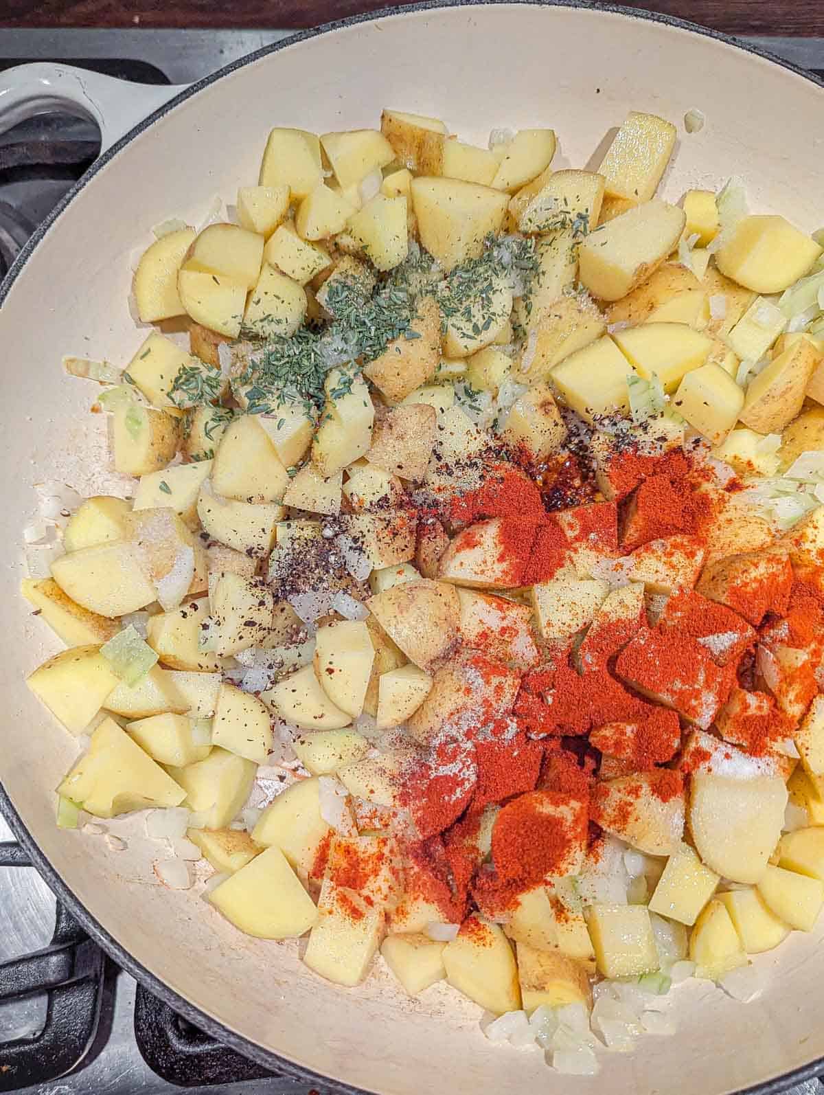 A large enameled cast iron pot containing cubed potatoes and finely diced onions along with seasonings.