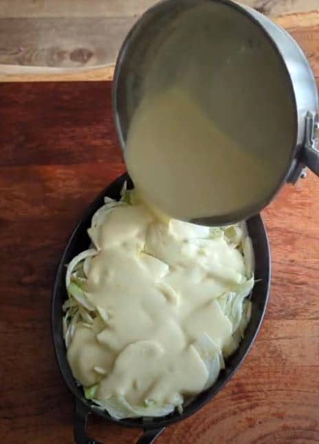 Pouring cheesy bechamel over fennel in a roasting dish to make fennel gratin.