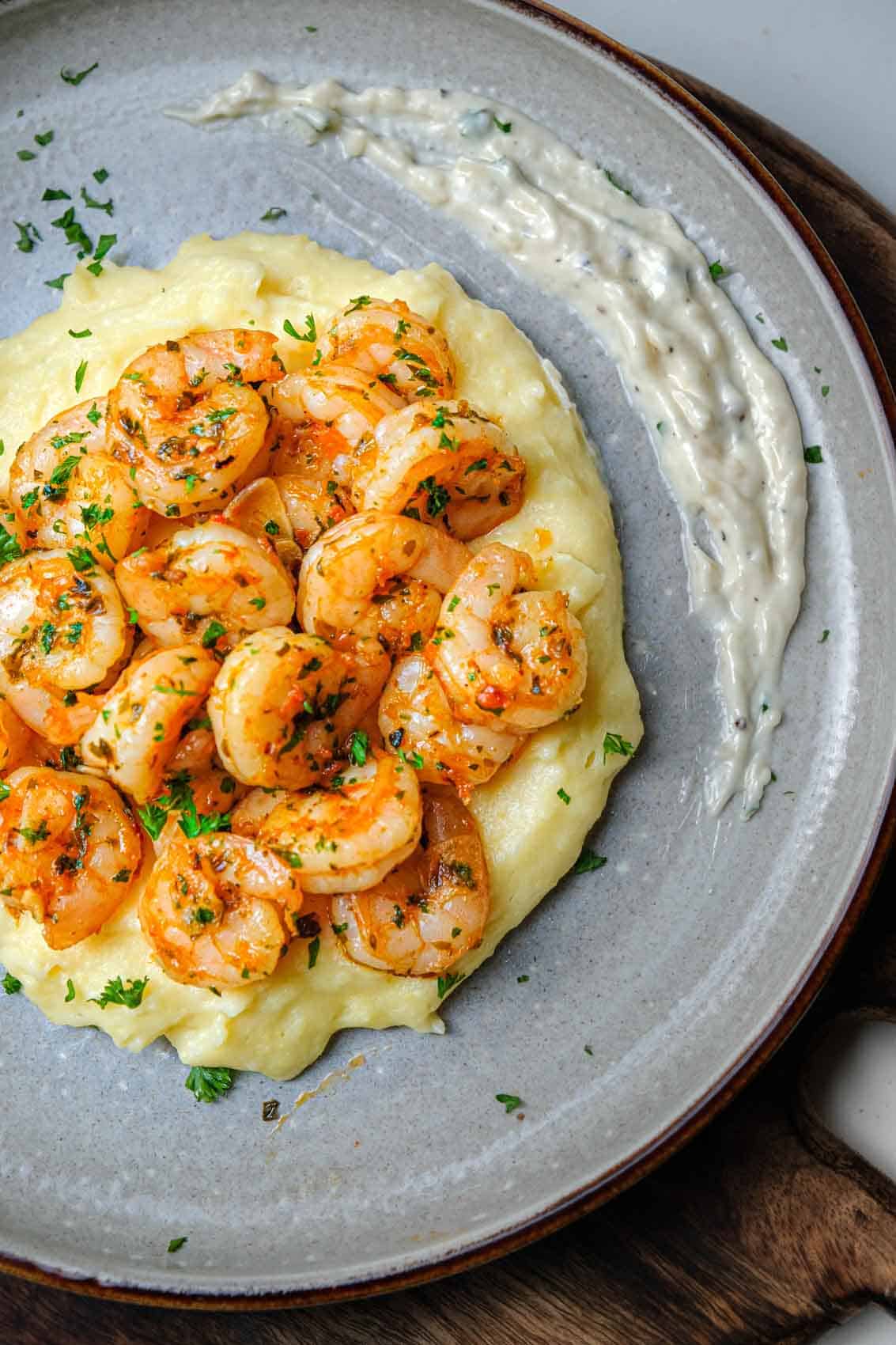 Closeup of a pile of red pepper shrimp on creamy polenta with a dollop of roasted garlic aioli