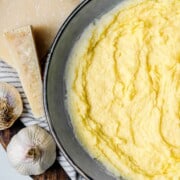 An overhead view of polenta in a bowl with a block of parmesan cheese and garlic bulbs in the background.