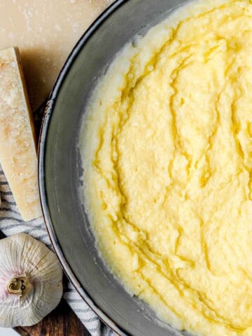 An overhead view of polenta in a bowl with a block of parmesan cheese and garlic bulbs in the background.
