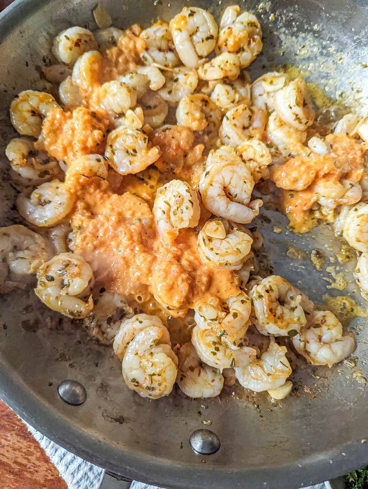 The seasoned shrimp cooking in a skillet with the red pepper sauce just added.